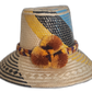 A colorful boho straw hat handmade by Wayuu artisans, featuring yellow, black, and blue patterns woven from Iraca palm with a pompom detail.