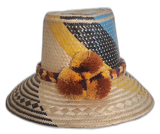 A colorful boho straw hat handmade by Wayuu artisans, featuring yellow, black, and blue patterns woven from Iraca palm with a pompom detail.