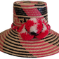Handmade Wayuu straw hat in pink, black, and beige with red pompoms.

