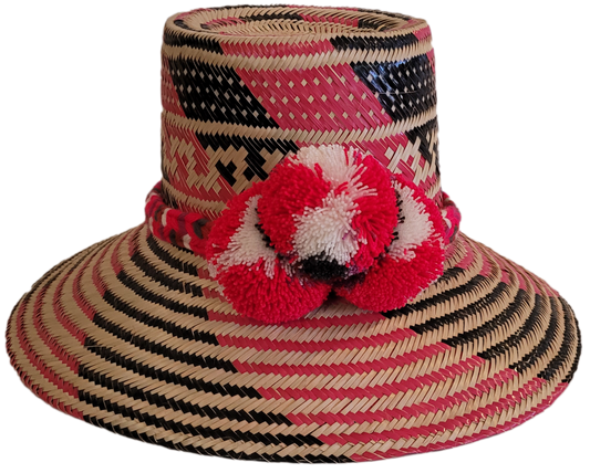 Handmade Wayuu straw hat in pink, black, and beige with red pompoms.

