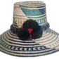 Boho straw hat handmade by Wayuu artisans, featuring blue and green woven designs with red-accented pompoms.