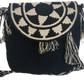 Handmade Wayuu crochet flap bag in black and beige with geometric tribal sunburst design and tassels — a bold artisan boho-chic essential.