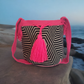 Handmade Wayuu crochet bag with black and beige geometric design, vibrant hot pink strap, and bold tassel — a colorful boho-chic statement piece.