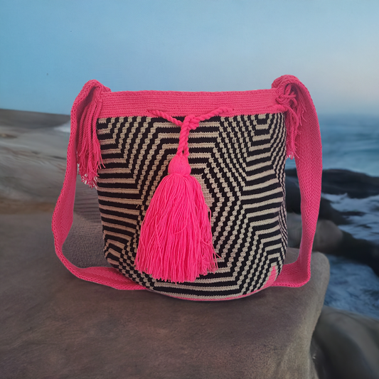 Handmade Wayuu crochet bag with black and beige geometric design, vibrant hot pink strap, and bold tassel — a colorful boho-chic statement piece.
