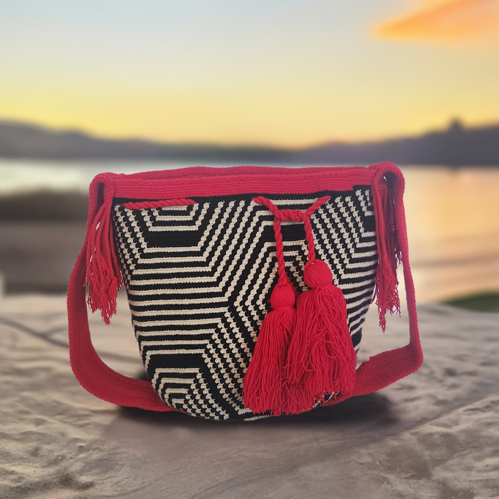 Boho-chic Wayuu crochet bag with bold black and white geometric pattern, vibrant red strap, and tassels — handmade artisan style with flair.