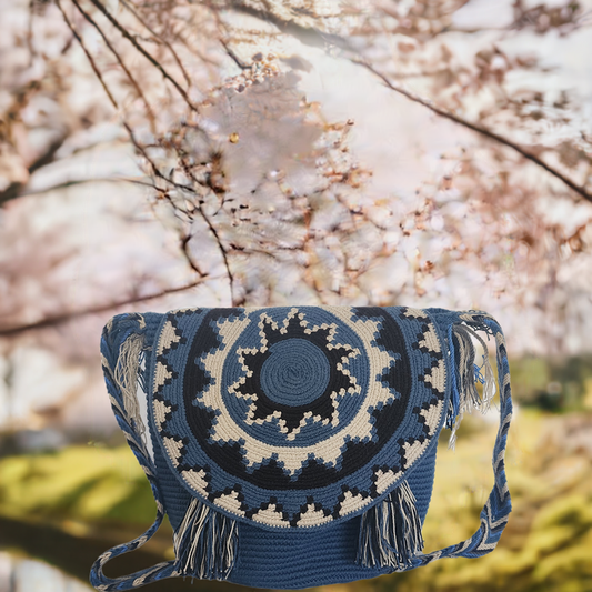 Handmade Wayuu crochet flap bag in blue and cream with sunburst pattern and fringe — a boho-chic artisan piece full of texture and tradition.