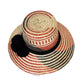 "Colorful, handmade straw hats by Wayuu tribe with adjustable sizes and meaningful pompoms, showcasing unique craftsmanship."