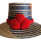 "Colorful handmade Wayuu hat woven from Iraca palm fibers, adorned with significant pompoms, adjustable for various sizes."
