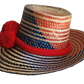 "Colorful handmade Wayuu hat woven from Iraca palm fibers, adorned with significant pompoms, adjustable for various sizes."