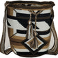 Earth-tone bohemian crochet bag, handmade by Wayuu artisans, featuring brown and cream weave, black accents, crossbody strap, and tassels.