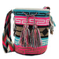 Bright bohemian crochet bag, handmade by Wayuu artisans, featuring vibrant pink and turquoise weave, patterned strap, and playful tassels.