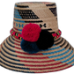 Gracie handmade Wayuu straw hat with bold black, blue, and red woven patterns and matching pompoms.

