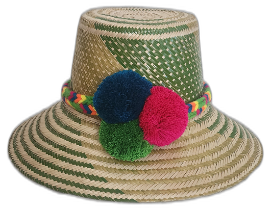Handmade Wayuu straw hat with green woven pattern and bold fuchsia, navy blue, and green pompoms.Bohemian Wayuu hat featuring green body and vibrant handmade pompoms