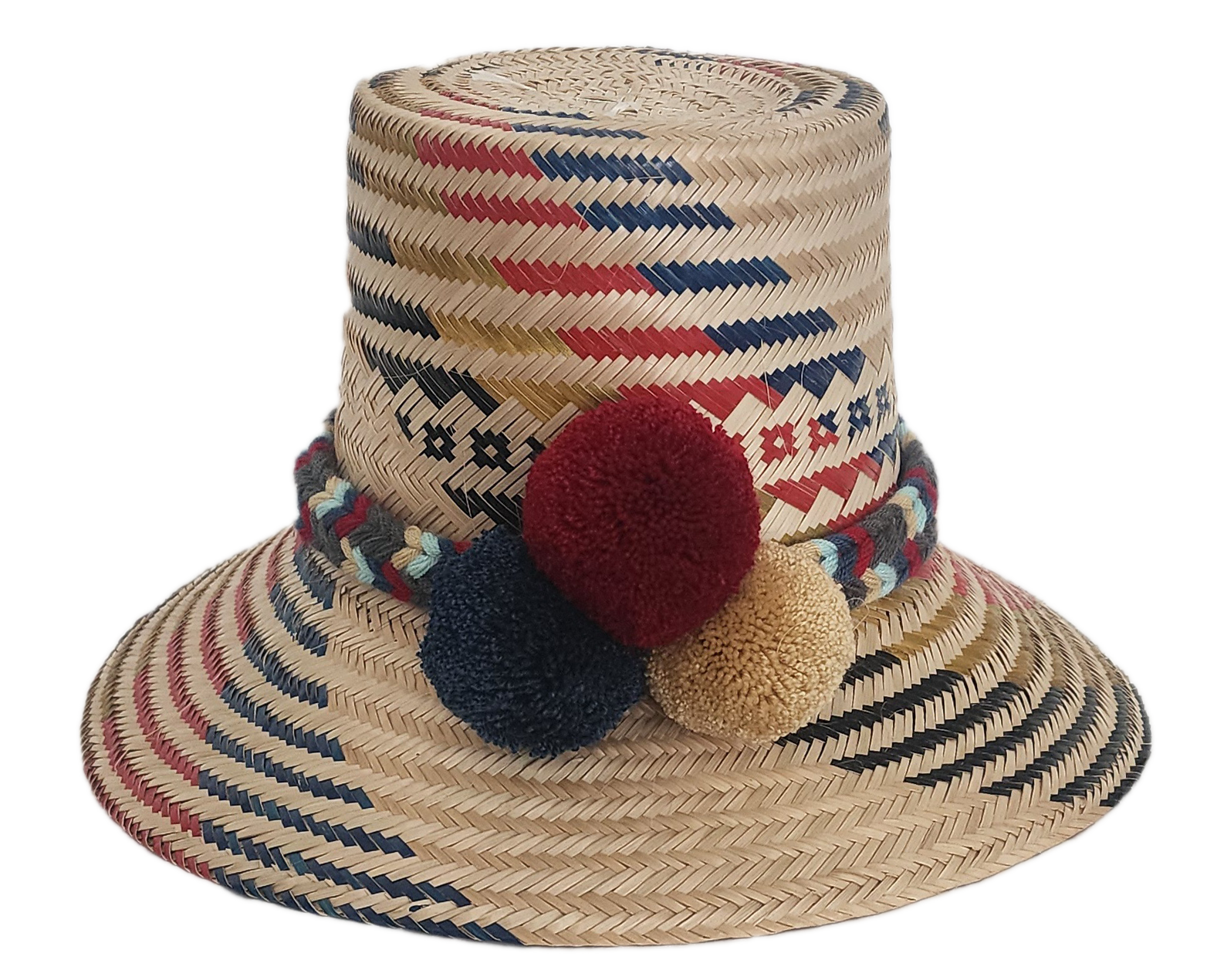 Handwoven Wayuu straw hat with red, navy, and golden zigzag patterns and a braided band finished with tri-color pom-poms. A bold, artisan-crafted boho hat.