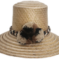 Handwoven Wayuu straw hat in a natural finish, featuring a braided band with earth-toned pom-poms in black, beige, and brown. A timeless boho accessory.