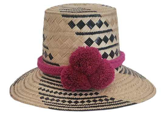 Wayuu handmade straw hat with magenta yarn pom-poms and black tribal patterns — boho and artisan-crafted.