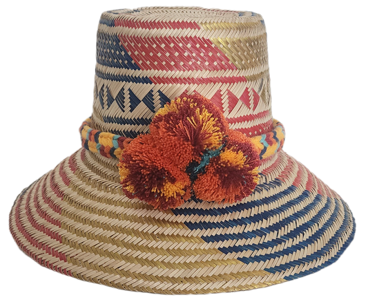 Handwoven Wayuu straw hat featuring red, navy, and golden tribal patterns, accented with a colorful braided band and vivid orange and maroon pom-poms.