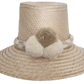 Handwoven Wayuu straw hat in soft beige tones, featuring a wide brim and braided band adorned with neutral cream and taupe pom-poms. Elegant boho style.