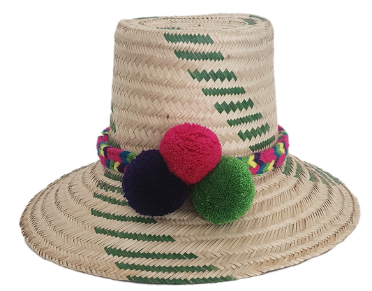 Handwoven Wayuu straw hat with green chevron patterns and a vibrant braided band, finished with red, green, and purple pom-poms. A playful boho accessory.