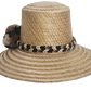 Handwoven Wayuu straw hat in a natural finish, featuring a braided band with earth-toned pom-poms in black, beige, and brown. A timeless boho accessory.