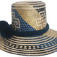 Artisan Wayuu straw hat with bold blue and cream geometric weaving, wide brim, and navy pom-pom band. A handcrafted boho accessory for standout summer style.