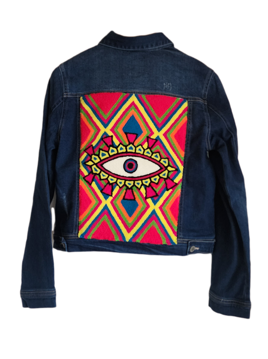 "Handmade denim jacket with colorful Wayuu-inspired punch needle embroidery on the back, showcasing unique bohemian style."