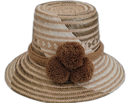 Handmade Wayuu straw hat in earthy beige tones with brown pompoms.

