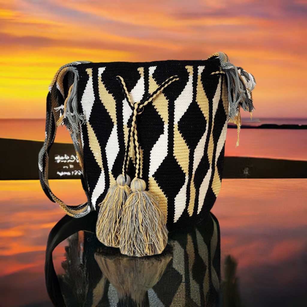 Handmade Wayuu crochet bag in black, tan, and white with wave-like diamond patterns, large coordinated tassels, and artisan-crafted crossbody strap.
