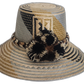 Handmade Wayuu straw hat with black and beige pompoms and geometric neutral design.Boho Wayuu hat with earth-toned colorblocking and cultural pattern
