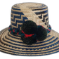 Handmade Wayuu straw hat with navy and black weave and dark green and red pompoms.Boho Wayuu hat featuring zigzag designs and handcrafted pompoms



