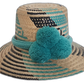 Handmade Wayuu boho straw hat with turquoise pompoms and bold black weave patterns.