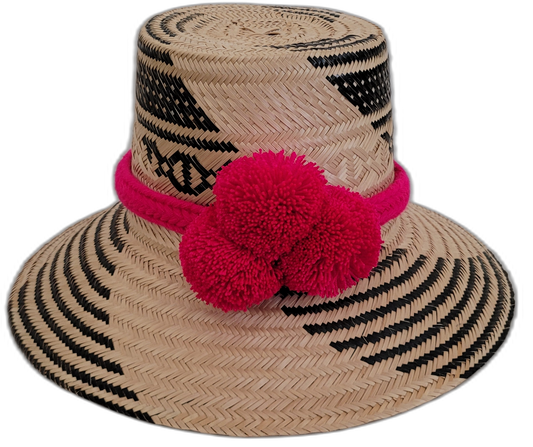 Handmade Wayuu straw hat with black and natural patterns, accented with hot pink pompoms.

