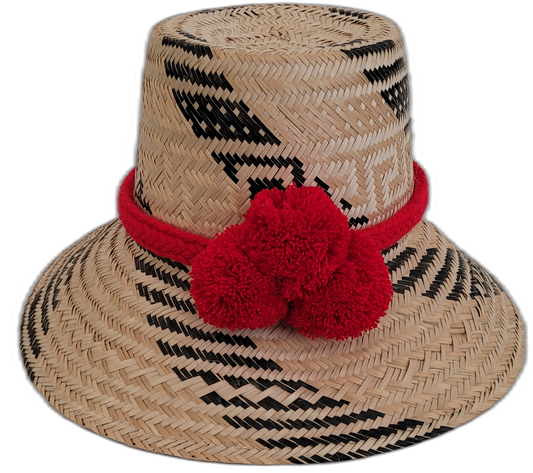 Handmade Wayuu straw hat with black and natural weave, accented by bright red pompoms.