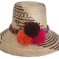 Handmade Wayuu straw hat with brown tribal designs and colorful pompoms