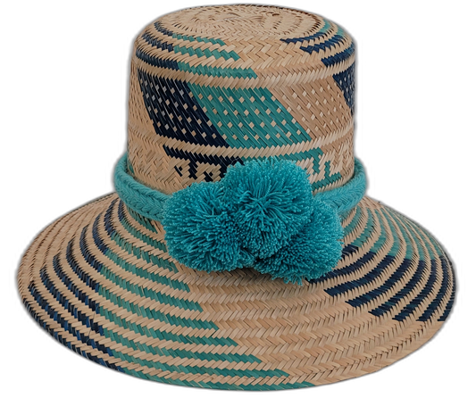 Handmade Wayuu straw hat with turquoise and navy patterns, accented with turquoise pompoms.

