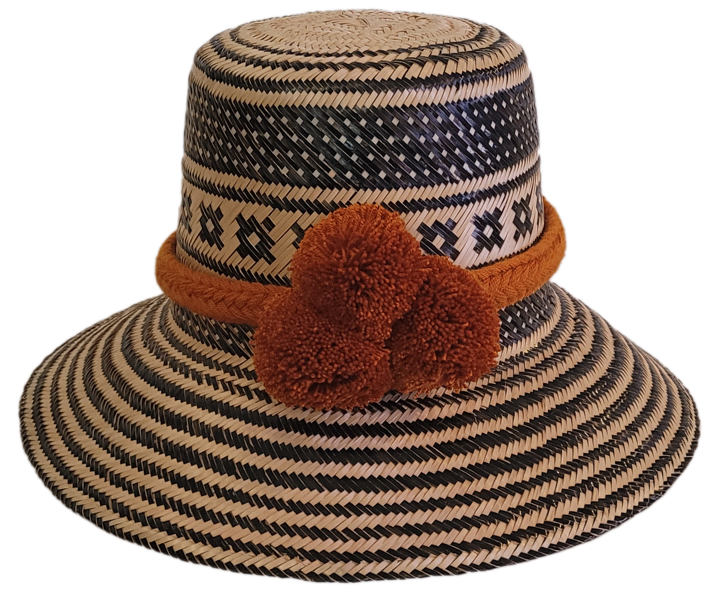 Handmade Wayuu straw hat with black geometric patterns and bold burnt orange pompoms — artisan boho accessory with cultural flair.
