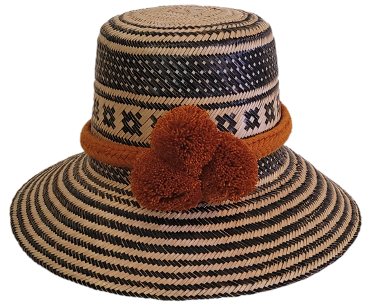 Handmade Wayuu straw hat with black geometric patterns and bold burnt orange pompoms — artisan boho accessory with cultural flair.