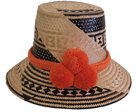 Handmade Wayuu straw hat in natural and black tones, featuring bold orange pompoms and tribal patterns — boho artisan piece for standout style.

