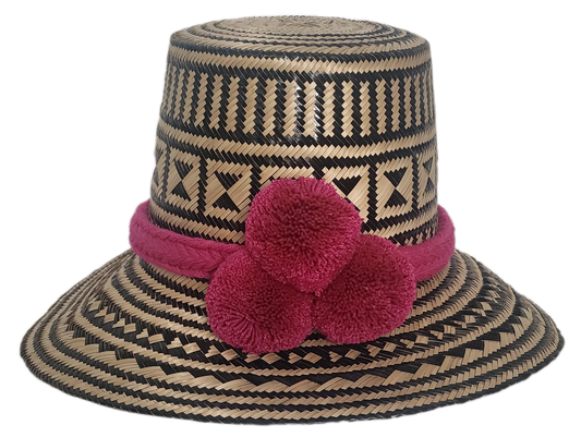 Handwoven Wayuu straw hat with black geometric patterns, vibrant pink braided band, and three matching handmade pink pom-poms.