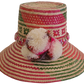 Colorful handmade Wayuu straw hat with pink, red, and green geometric patterns and multicolor pom-poms — artisan boho accessory for women.
