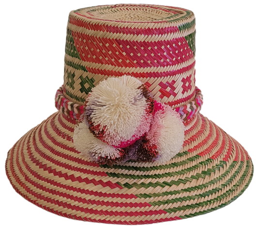 Colorful handmade Wayuu straw hat with pink, red, and green geometric patterns and multicolor pom-poms — artisan boho accessory for women.