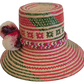 Boho chic Wayuu hat, handwoven from Iraca palm with vibrant red and green patterns and decorative cream and pink pompoms — perfect for summer style.