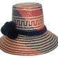 Colorful artisan straw hat handmade by Wayuu weavers, featuring diagonal red and blue designs with a dark blue pom-pom accent and wide brim.