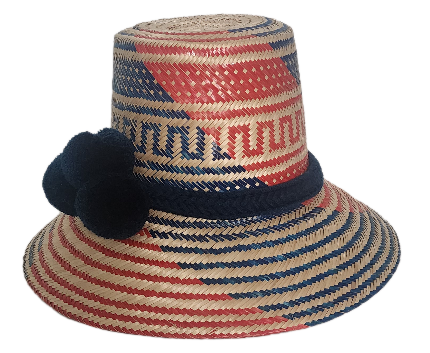 Colorful artisan straw hat handmade by Wayuu weavers, featuring diagonal red and blue designs with a dark blue pom-pom accent and wide brim.