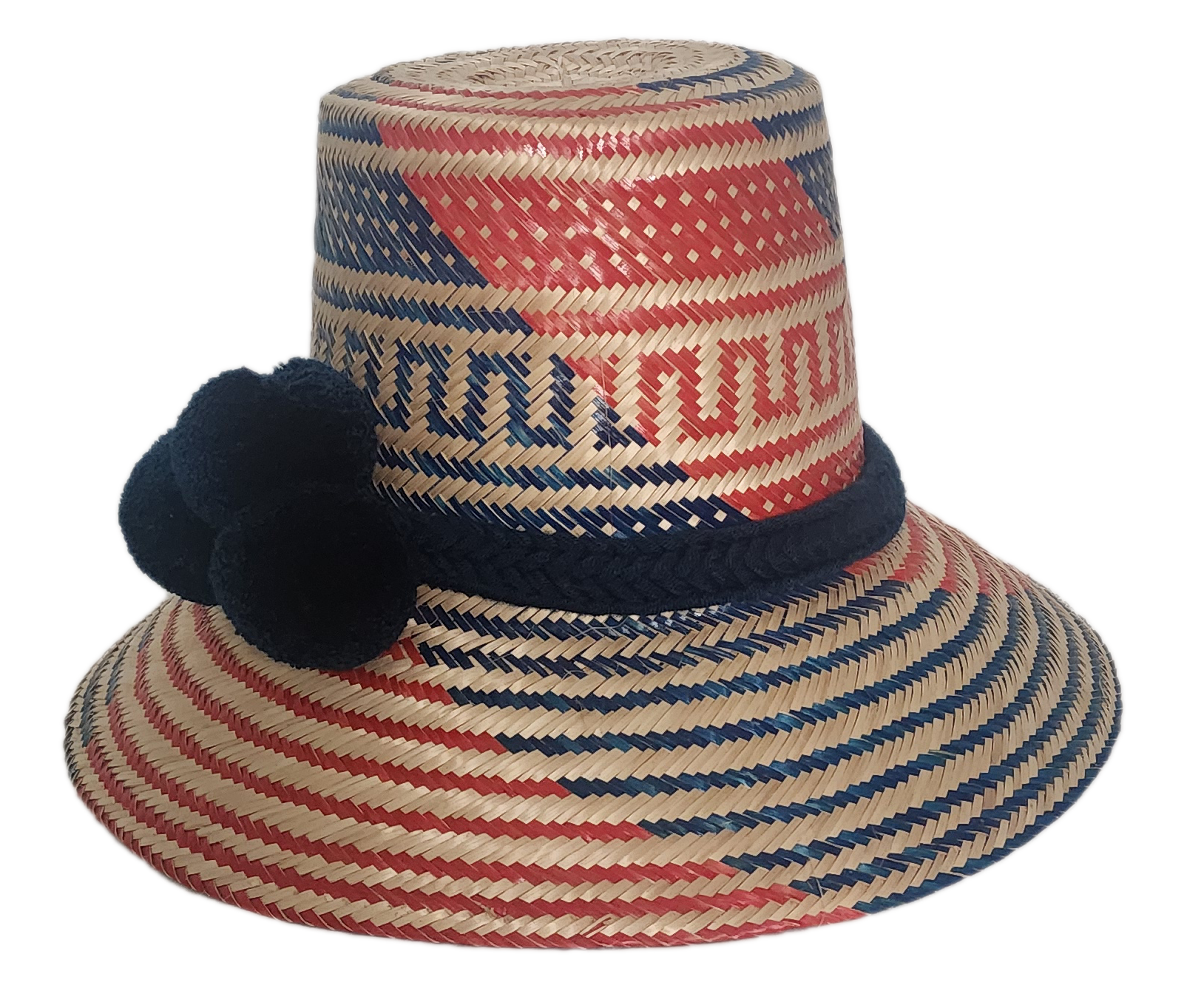 Colorful artisan straw hat handmade by Wayuu weavers, featuring diagonal red and blue designs with a dark blue pom-pom accent and wide brim.