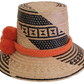 Bohemian-style artisan Wayuu hat with natural weave, black geometric accents, and vivid orange pom-poms — handcrafted for vibrant boho looks.
