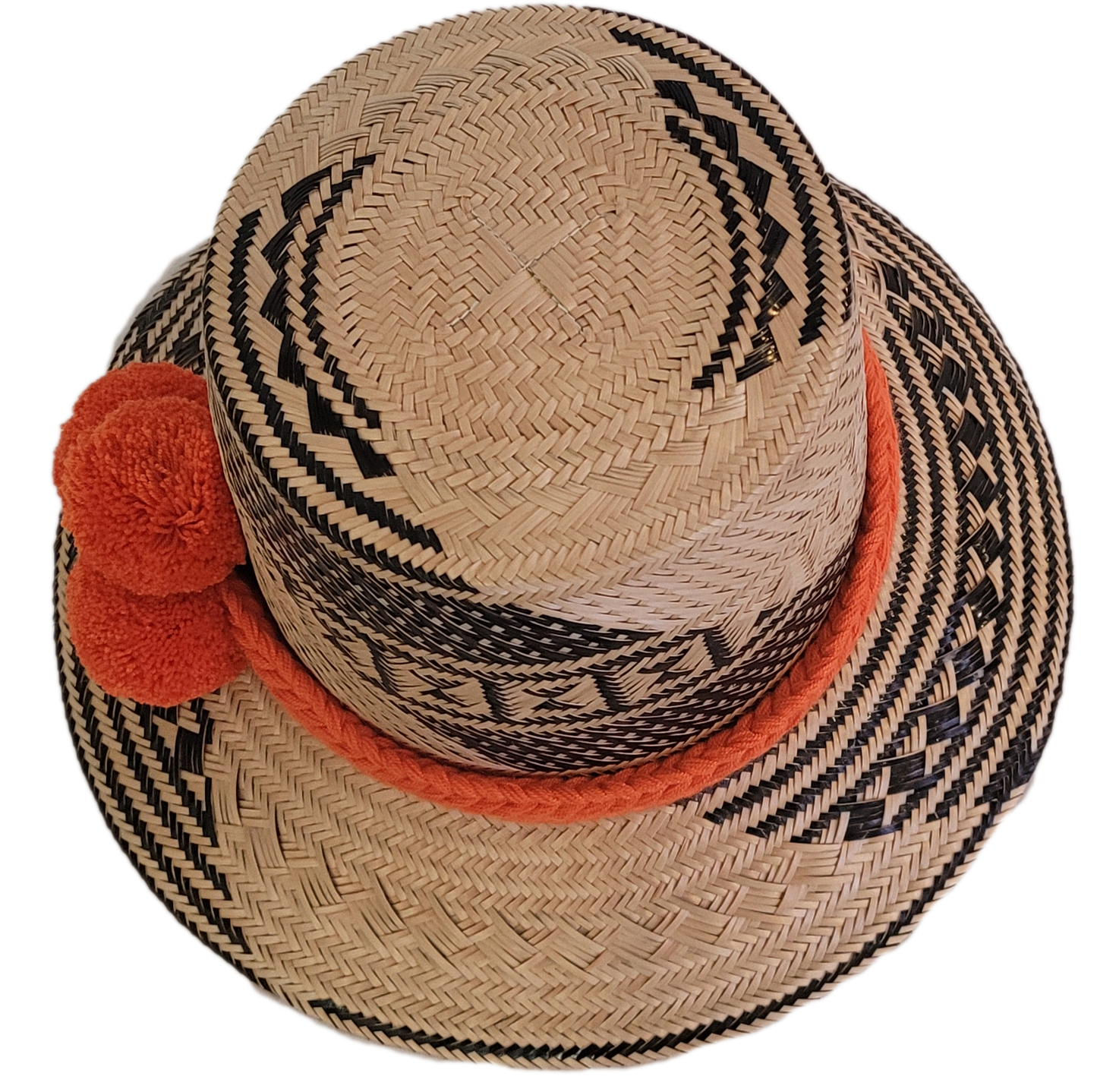 Black and beige Wayuu straw hat with a bright orange braided band and pompoms — a colorful, handmade boho accessory full of artisan charm.
