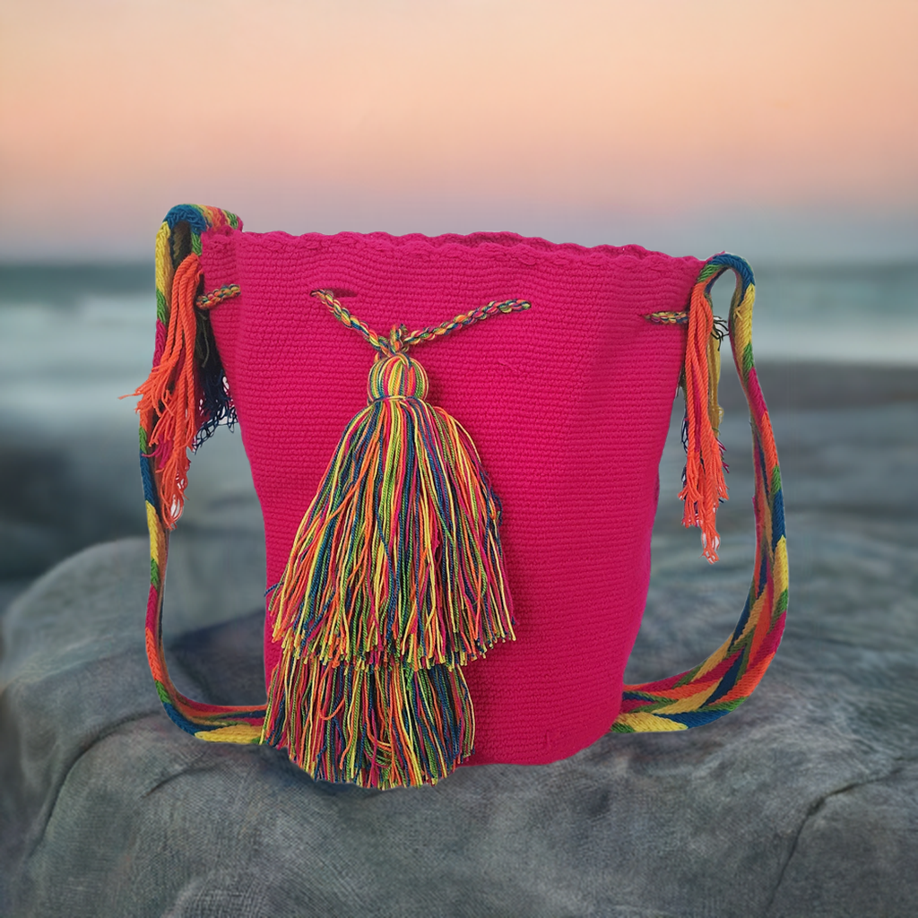 Hot pink handmade Wayuu crochet bag with vibrant rainbow tassels and multicolor strap — bold Boho fashion.
