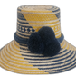 Handmade bohemian straw hat in navy and yellow with pompoms, crafted by Wayuu artisans.Boho straw hat with bold blue pompom trio and golden zigzag pattern

