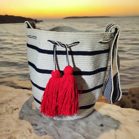 Handmade Wayuu crochet bag in white with navy stripes and red tassels.